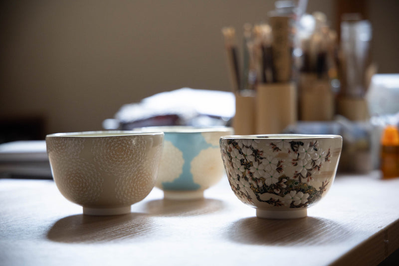 右は、桜雲茶盌。桜の花びらに立体感があって華やか。左の二点は、工程の途中にある、白菊蒼穹の茶盌。釉薬をかけて焼成した茶盌に下絵を写し、白菊を描き入れて焼成し、青い色を入れたら、また焼成する。